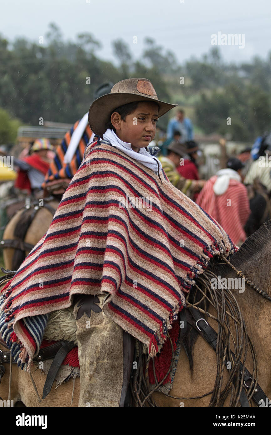 Juni 10, 2017 Toacazo, Ecuador: junge kichwa Jungen tragen ein Poncho zu Pferd im Regen an einer landwirtschaftlichen Rodeo Stockfoto