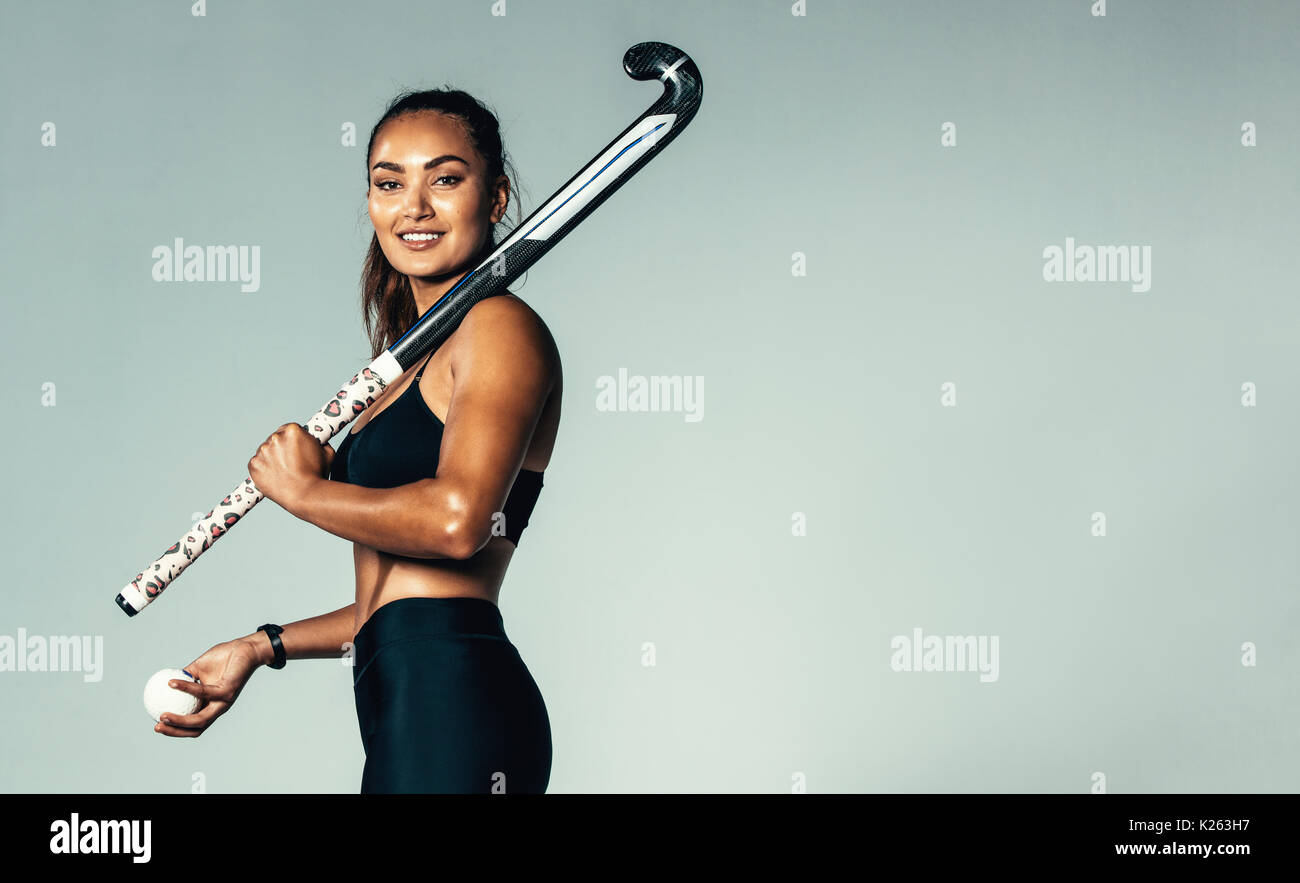 Porträt der schönen jungen Frau mit Hockey Stick und Kugel gegen grauen Hintergrund. Hispanic weiblichen Hockey Player auf Kamera. Stockfoto