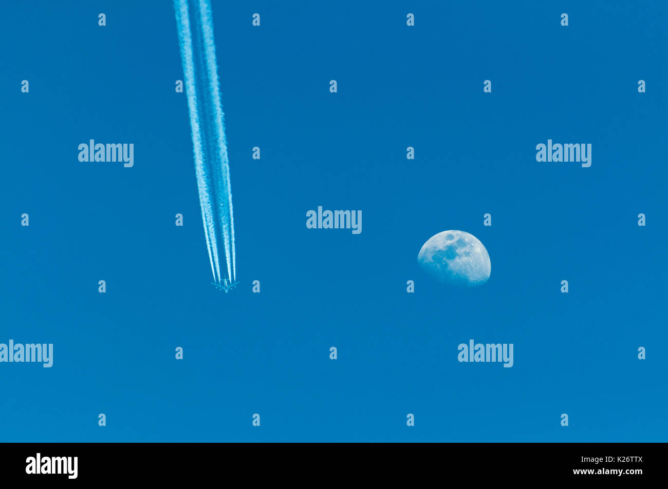 Flugzeug mit Kondensstreifen und Mond am blauen Himmel Stockfoto