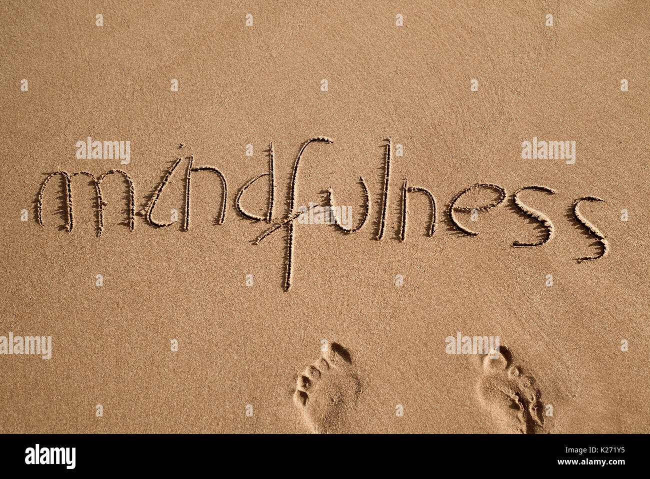 High-Angle Shot des Wortes Achtsamkeit in den Sand des Strandes geschrieben und ein paar menschliche Fußabdrücke Stockfoto