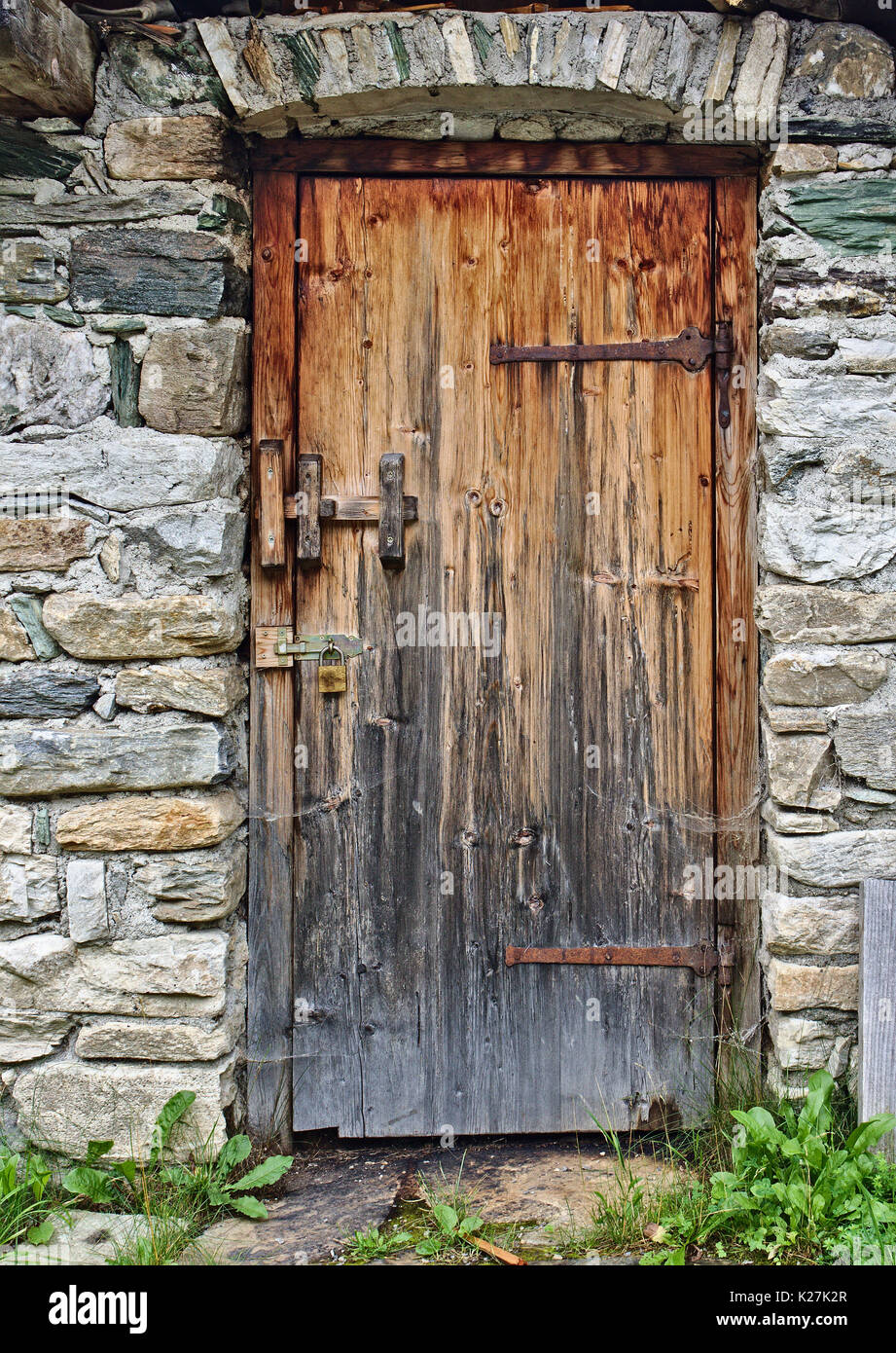 Alte Holztür im Feld Steinmauer mit großen rostigen Scharniere und Vorhängeschloss Stockfoto