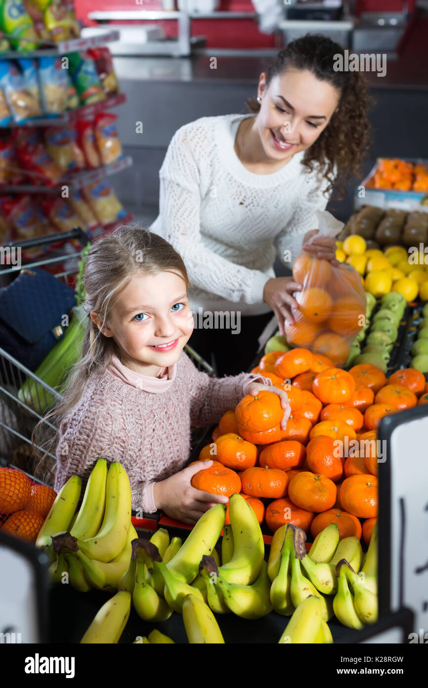 Fröhliche junge Frau und kleines Mädchen Einkauf süßen Mandarinen am Markt. Fokus auf Mädchen Stockfoto