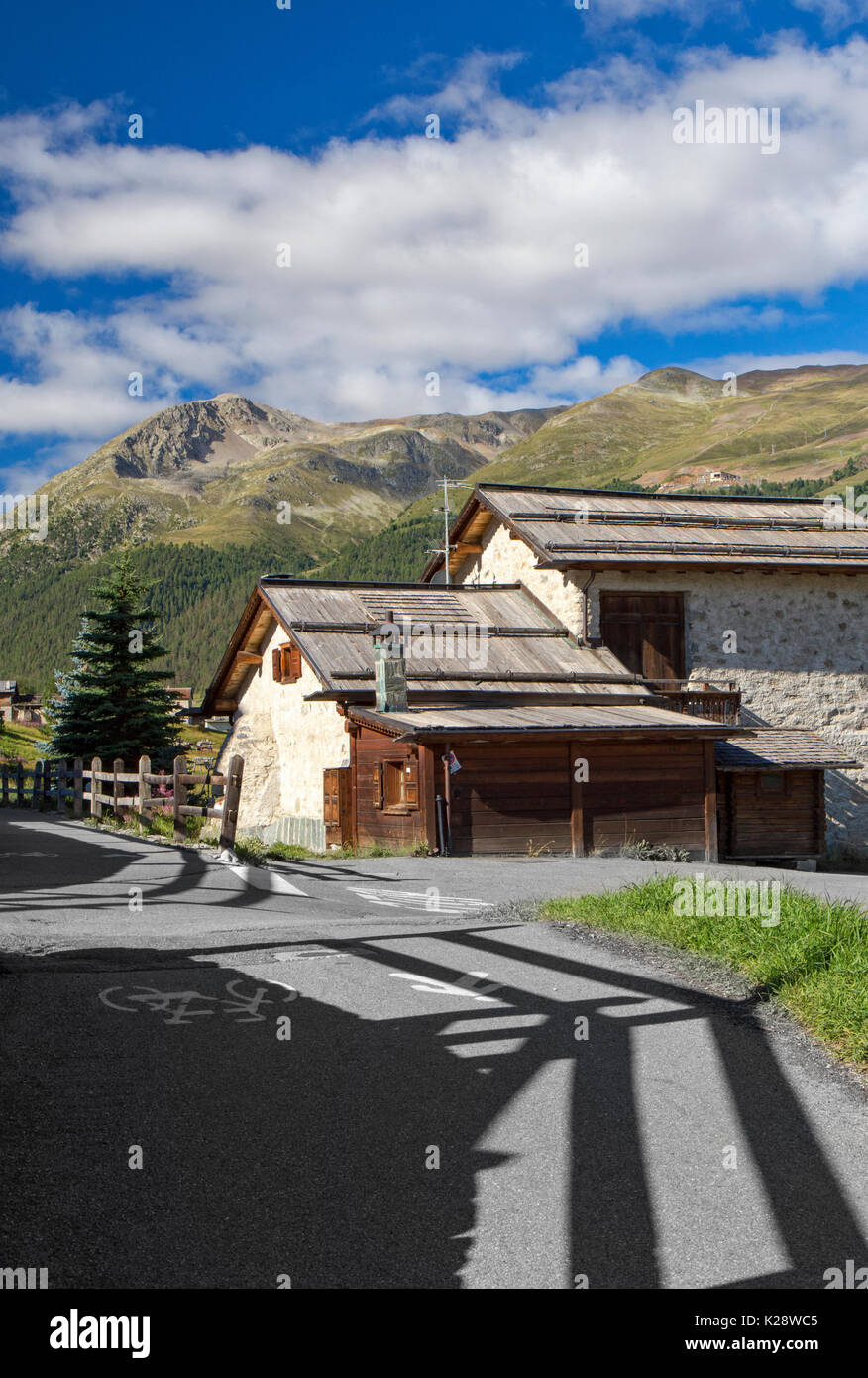 Braun historischen alten Holz und Stein Haus neben schwarzen Asphalt gepflasterte Straße mit grünem Gras und blauer Himmel meistens von Wolken bedeckt Stockfoto