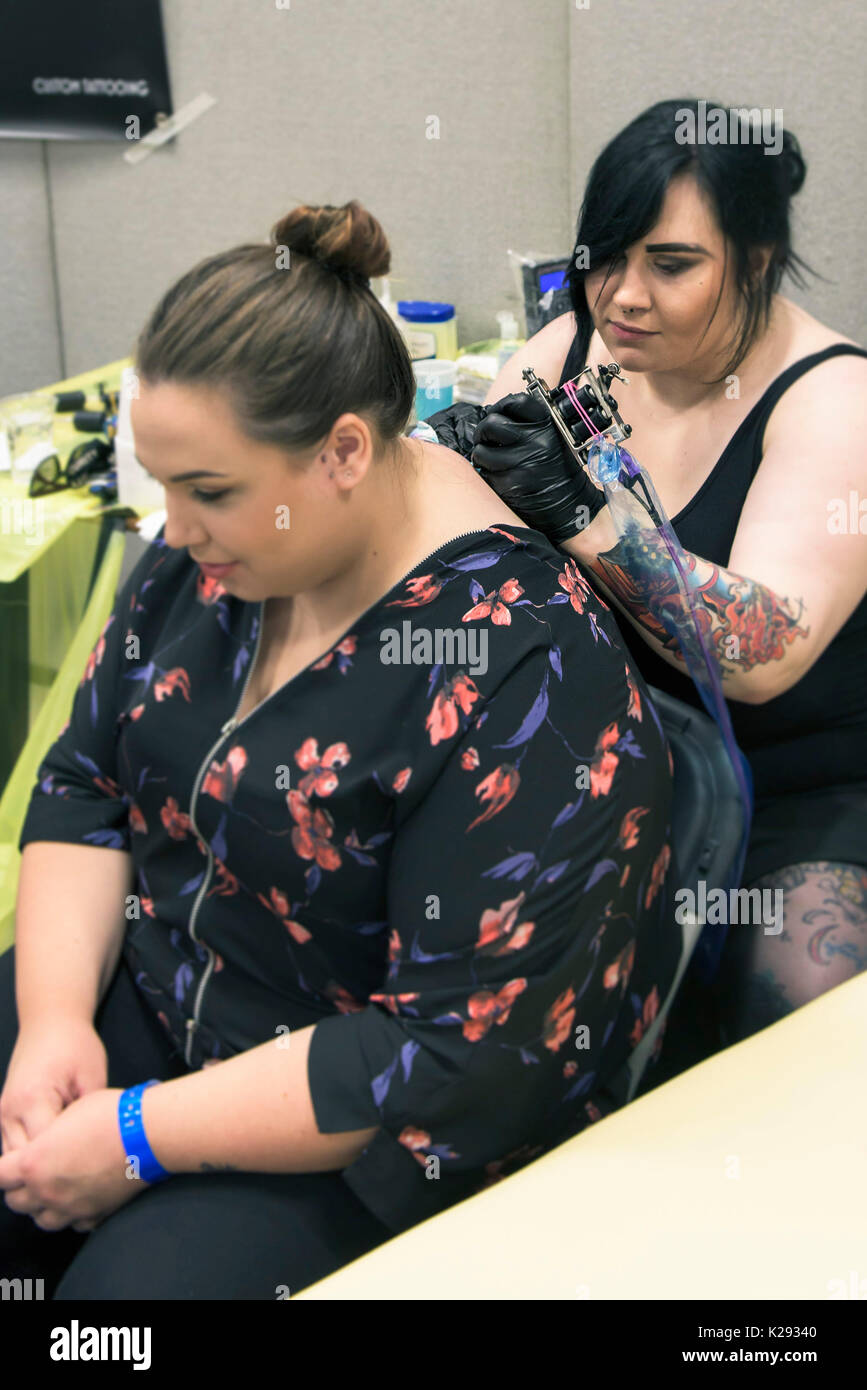 Cornwall Tattoo Convention - das weibliche Tätowierer Laura G Anwendung eine Tätowierung auf dem Rücken eines weiblichen Kunden am Cornwall Tattoo Convention. Stockfoto