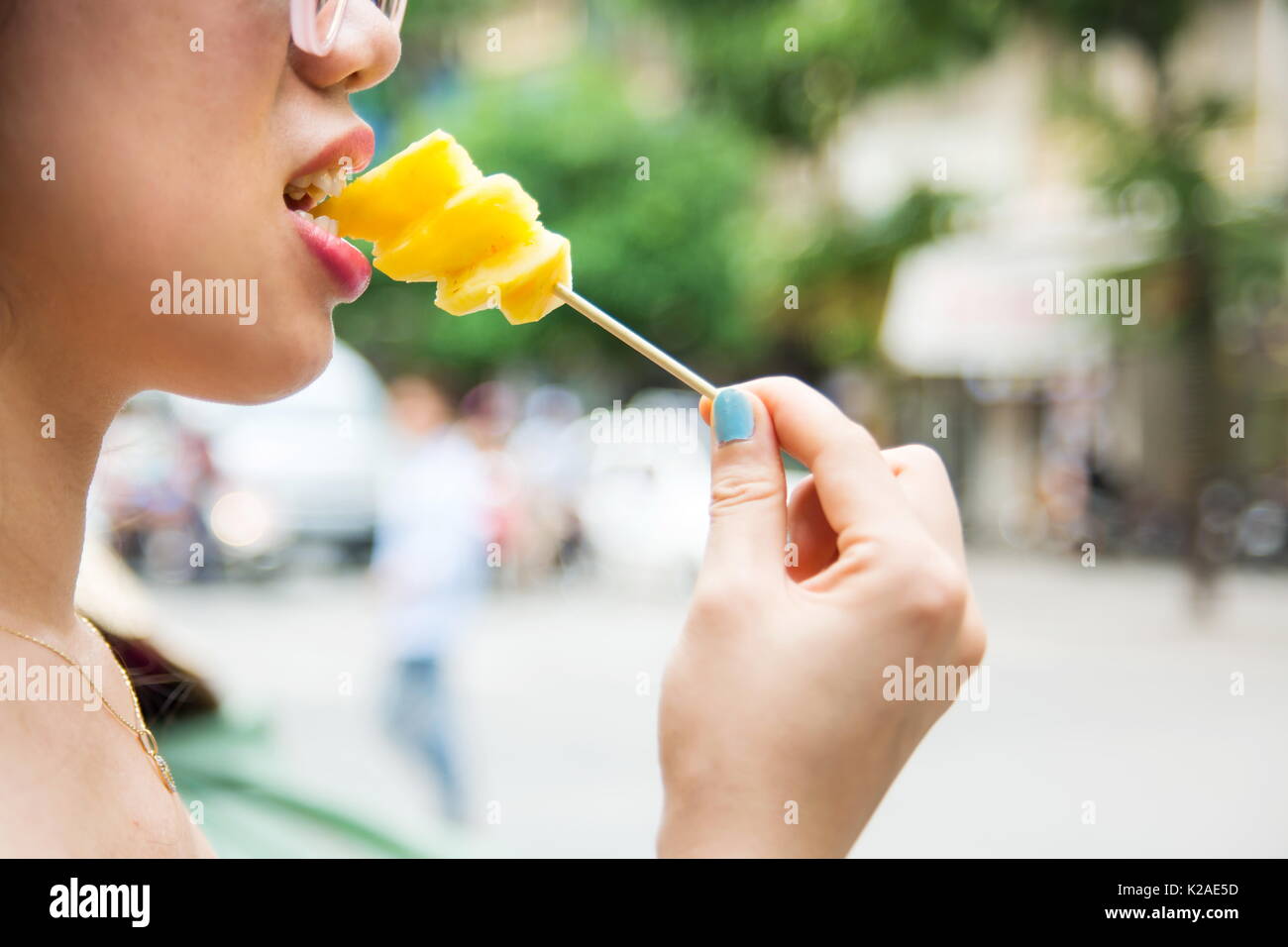Frau essen Ananasscheibe aus dem Stick Stockfoto