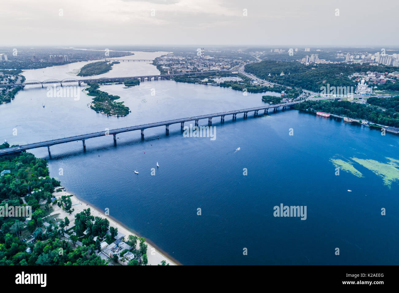 Panoramablick auf die Stadt Kiew mit dem Dnjepr in der Mitte. Luftaufnahme der Wohnviertel und industriellen Zone bei Sonnenuntergang. Zwei Banken des Stockfoto
