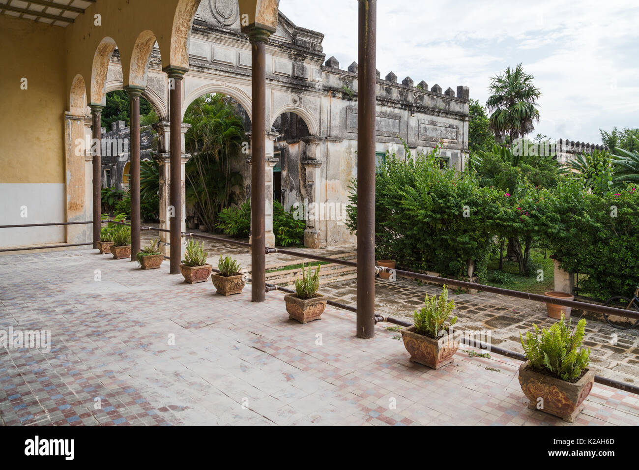 Ein Blick auf den Garten mit üppigen Büschen und Palmen aus der überdachten Terrasse im Hacienda Yaxcopoil, Yaxcopoil, Yucatan, Mexiko gefüllt. Stockfoto