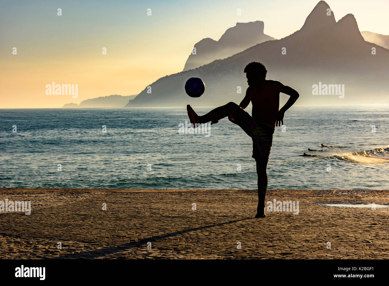 Junge spielt Fußball vor dem Meer bei Sonnenuntergang Stockfoto