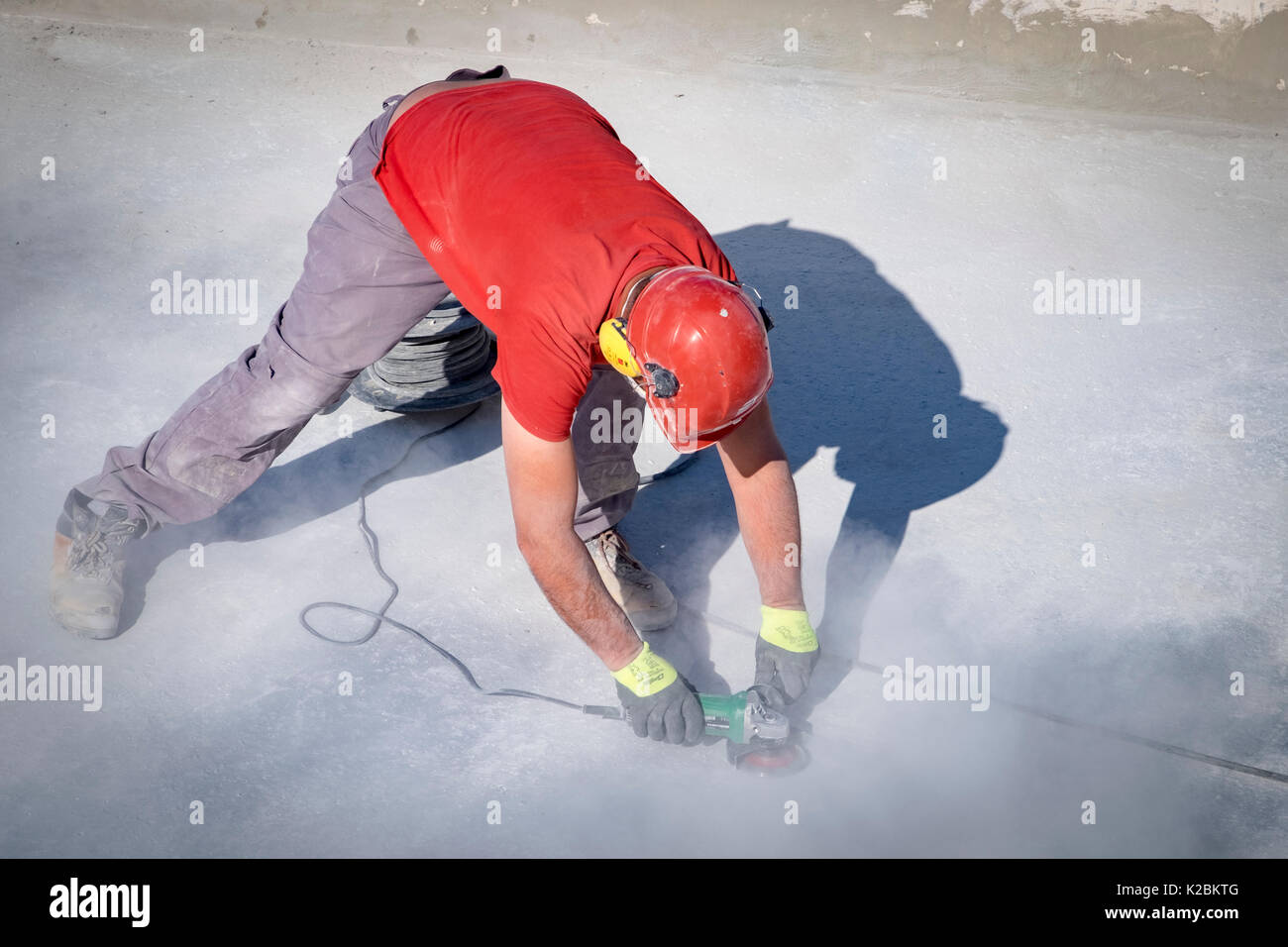 Bauarbeiter das Tragen von Helm und Kopfhörer verwendet eine Sander den Boden eines Pool Sand Stockfoto
