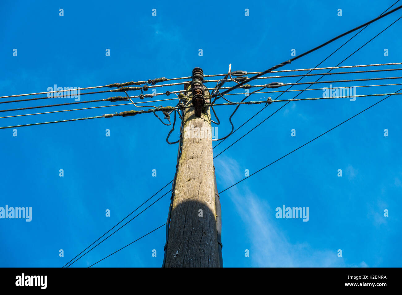 Eine Vertraute, Traditionelle, sonnendurchfluteten Telegraphenmast und Telefon Kabel, gesehen von unten, gegen ein strahlend blauer Himmel. Langtoft, Lincolnshire, England, UK. Stockfoto