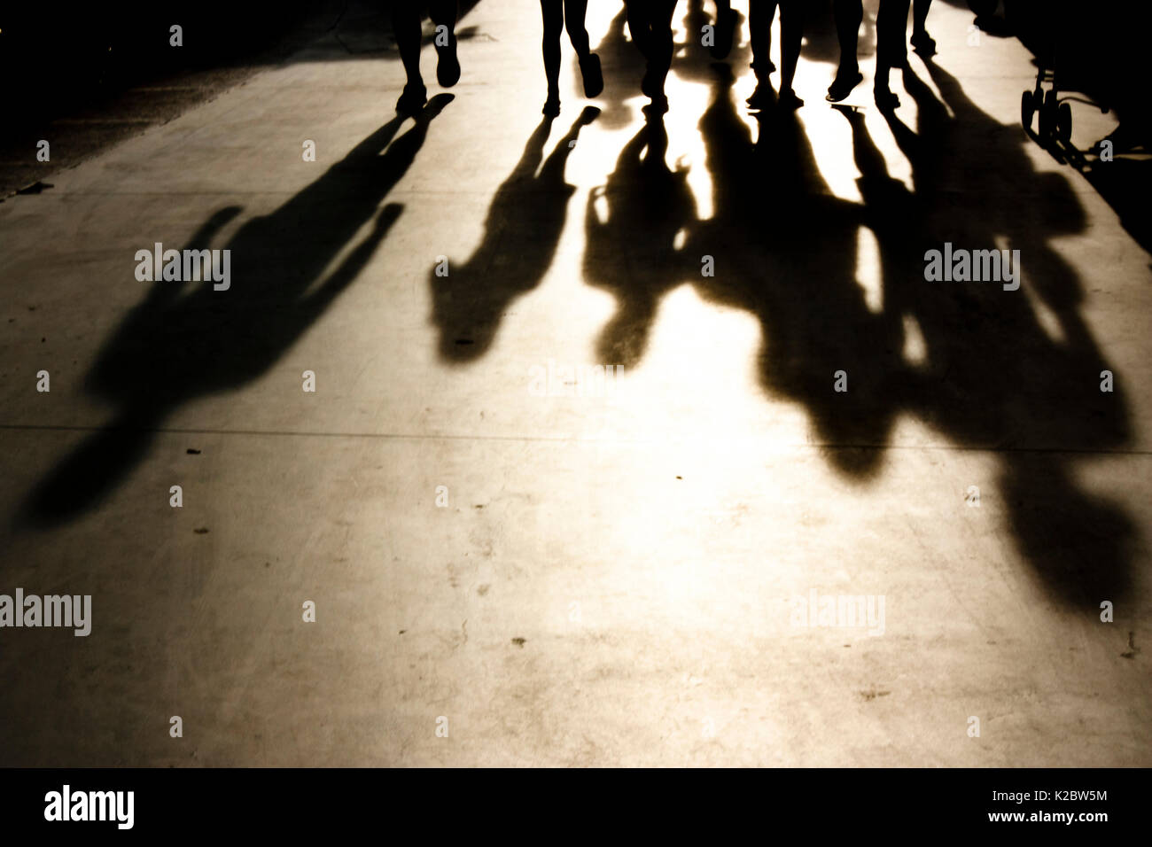 Verschwommene Schatten von Menschen zu Fuß in Richtung der Kamera an der Strandpromenade in misty Sommer Sonnenuntergang in Schwarz und Weiß Stockfoto