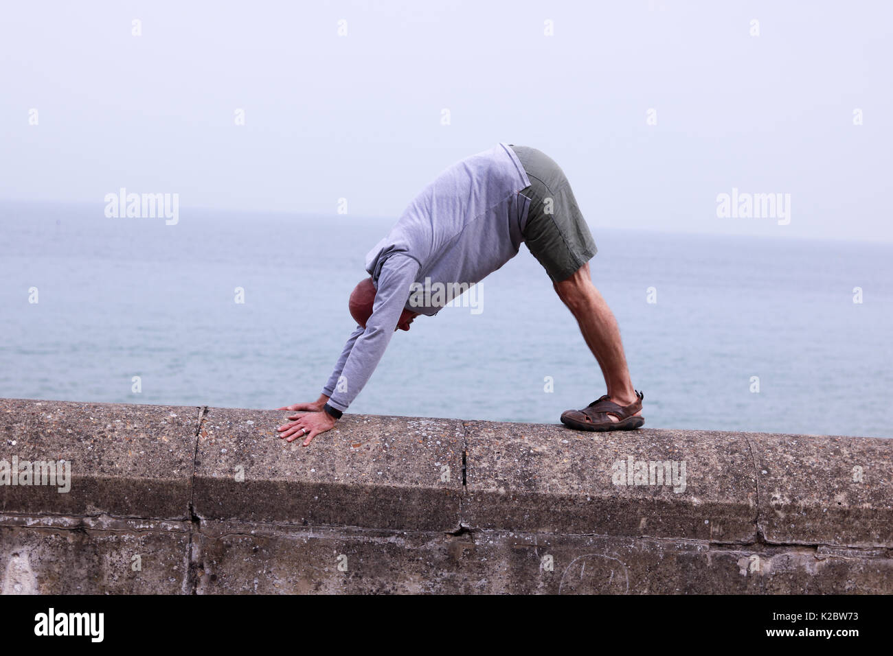 50 Jahre alter Mann einen nach unten schauender Hund yoga Pose auf Sea Wall  in Cromer, Norfolk, Großbritannien Stockfotografie - Alamy