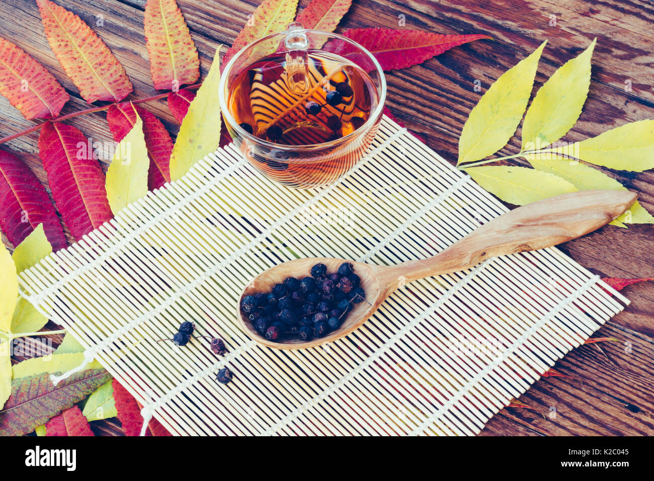 Getränk aus getrockneten Weißdorn-Beeren in hölzernen Löffel auf dem Tisch mit der bunten Blätter im Herbst. Ansicht von oben Nahaufnahme. Gefärbtes Bild. Herbst Konzept Stockfoto