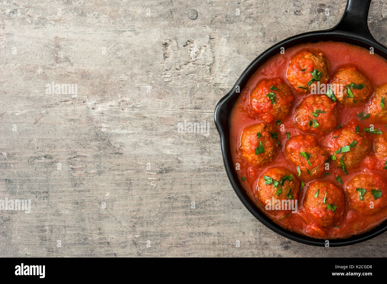 Hackfleischbällchen mit Tomatensauce in Eisenpfanne auf Holztisch. Ansicht von oben Stockfoto
