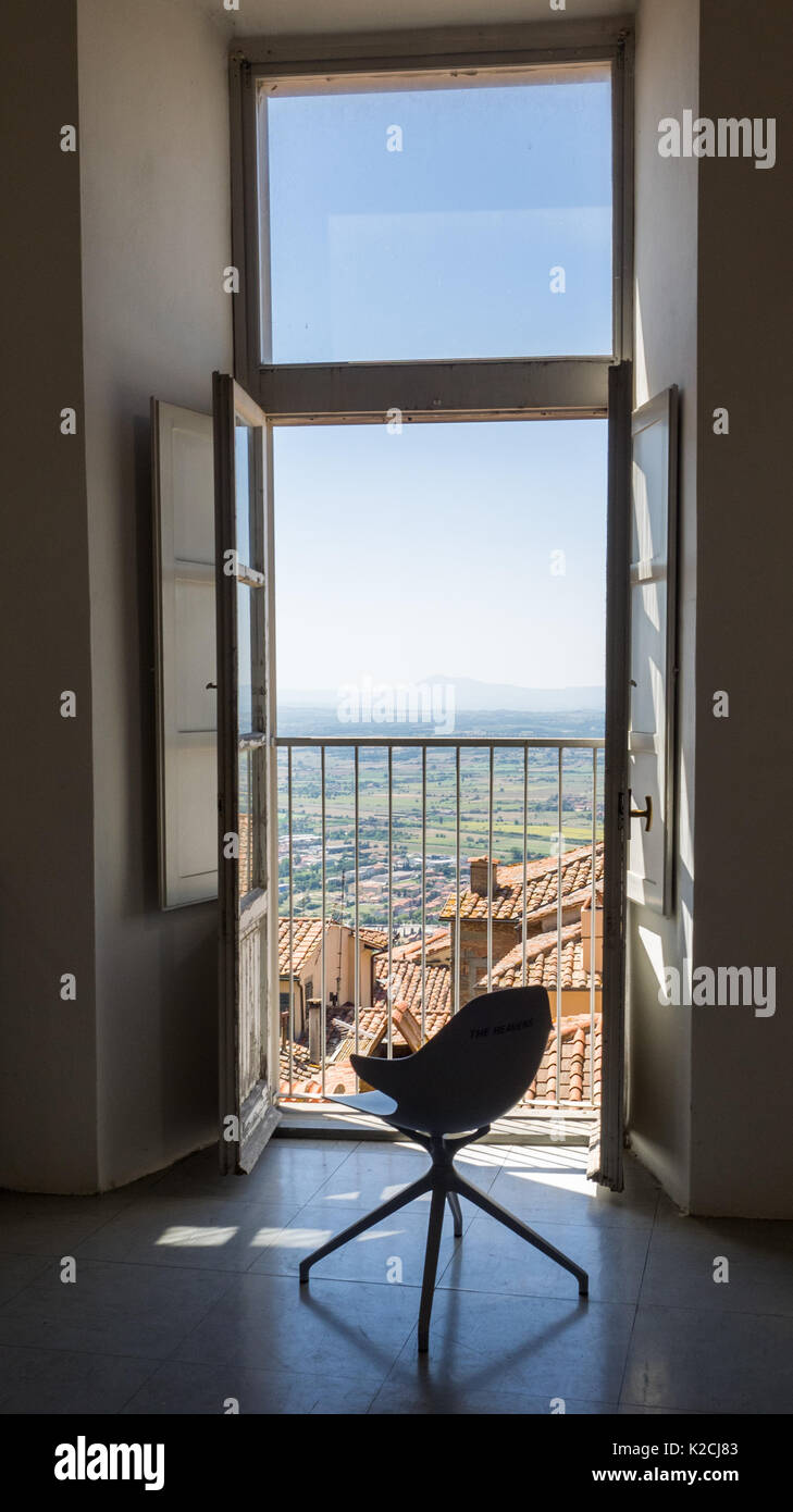 Eine leere moderner Drehstuhl durch ein offenes Fenster Türen, die auf einen Balkon mit Blick auf den klaren, blauen Himmel Horizont über dachlandschaft Stockfoto