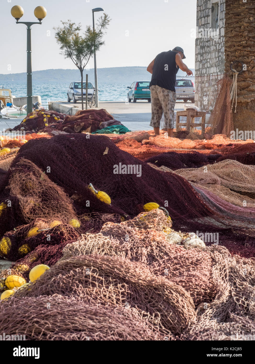 ein Fischer stehen nähen, ausbessern, Reparatur von seinem Netto Fischernetze mit Nadel und Faden am Kai am Meer, Kroatien Stockfoto