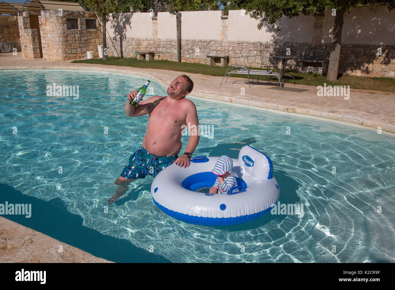 Ein betrunkener Vater im Urlaub mit seinem Kleinkind in einem Schwimmbad. Stockfoto