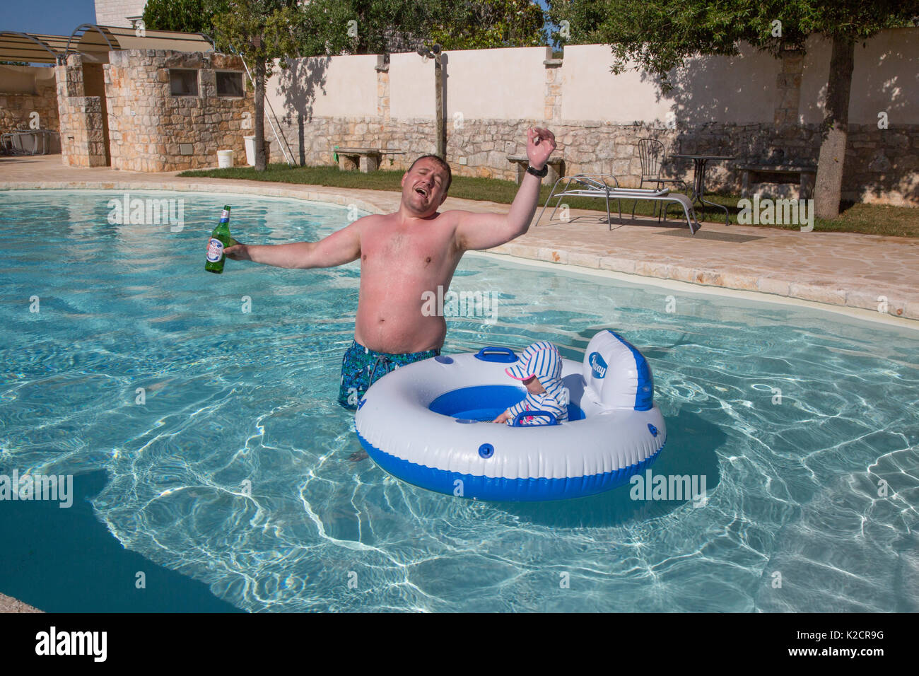Ein betrunkener Vater im Urlaub mit seinem Kleinkind in einem Schwimmbad. Stockfoto