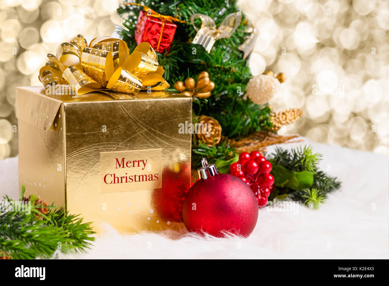 Glänzendes gold Geschenkbox mit Frohe Weihnachten Wort mit rot Deko Kugel, Kiefer code und Xmas Tree auf weißem Fell mit Glanz Gottes Licht bokeh Hintergrund, Wi Stockfoto