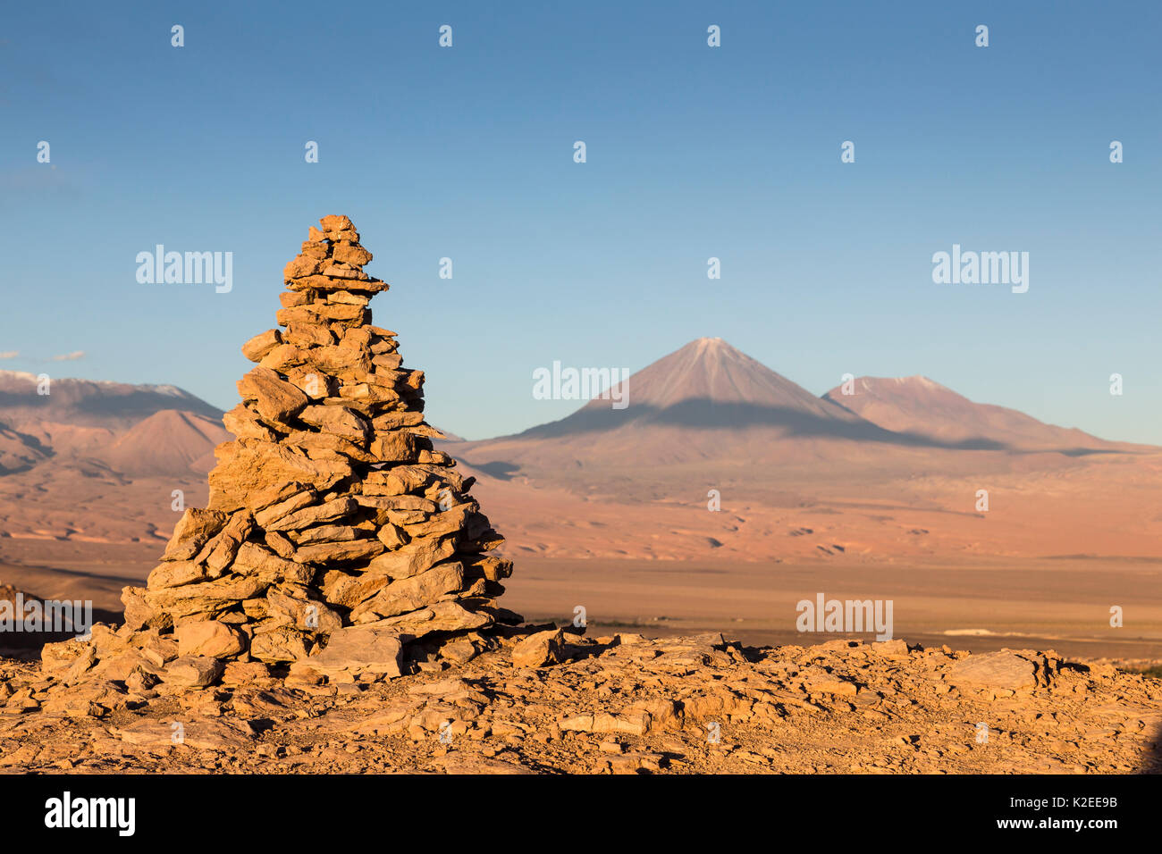 Apacheta/Apachita - ein Stein Cairn in den Anden, ein kleiner Haufen von Steinen auf dem Weg in den hohen Bergen mit Licancabur Vulkan gebaut (5916 m über dem Meeresspiegel) und Juriques Vulkan auf der rechten Seite (5704 m) im Hintergrund, Atacama, San Pedro, Chile Stockfoto