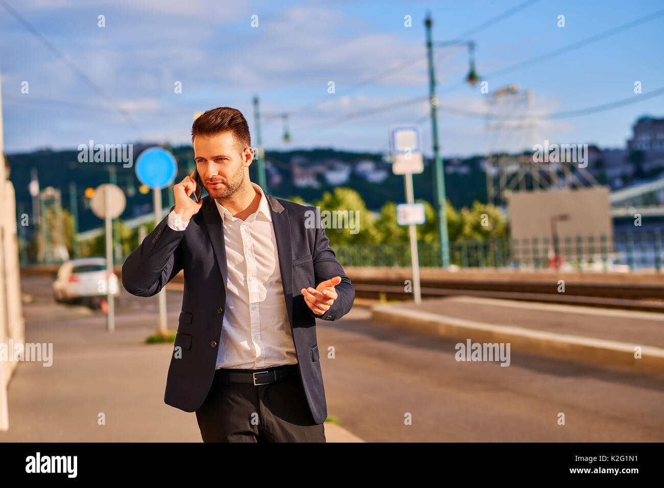 Ein hübscher junger Unternehmer gehen auf die Straße am Fluss, der gerade sein Telefon Stockfoto