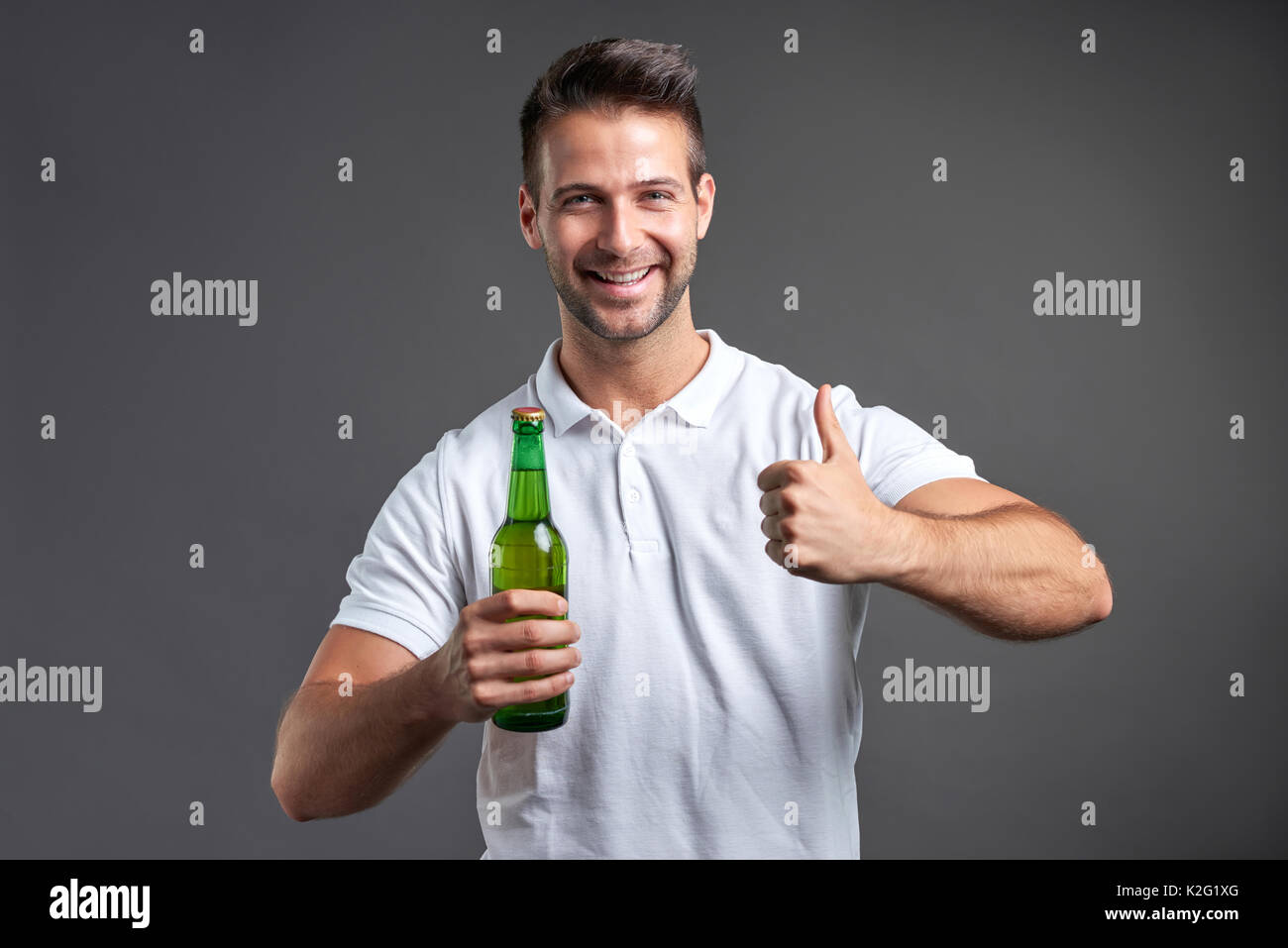 Ein hübscher junger Mann glücklich zeigen Daumen und halten Sie eine Flasche Bier Stockfoto