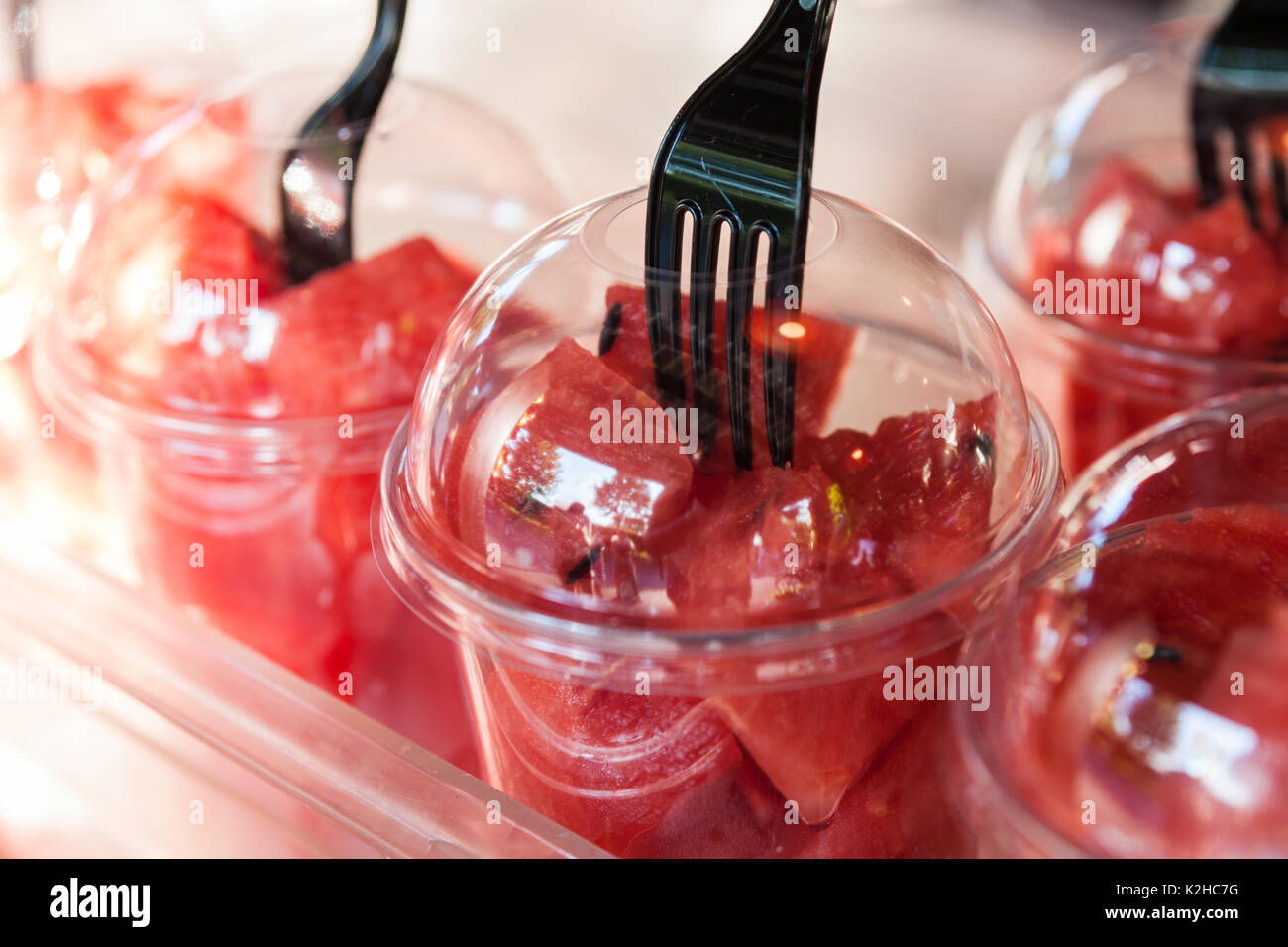 Gruppe aus transparentem Kunststoff Gläser, mit Wassermelone Stück gefüllt, auf Anzeige zum Verkauf an einem geöffneten Snackbar. Schwarz Gabel klemmt in Stücke. Stockfoto