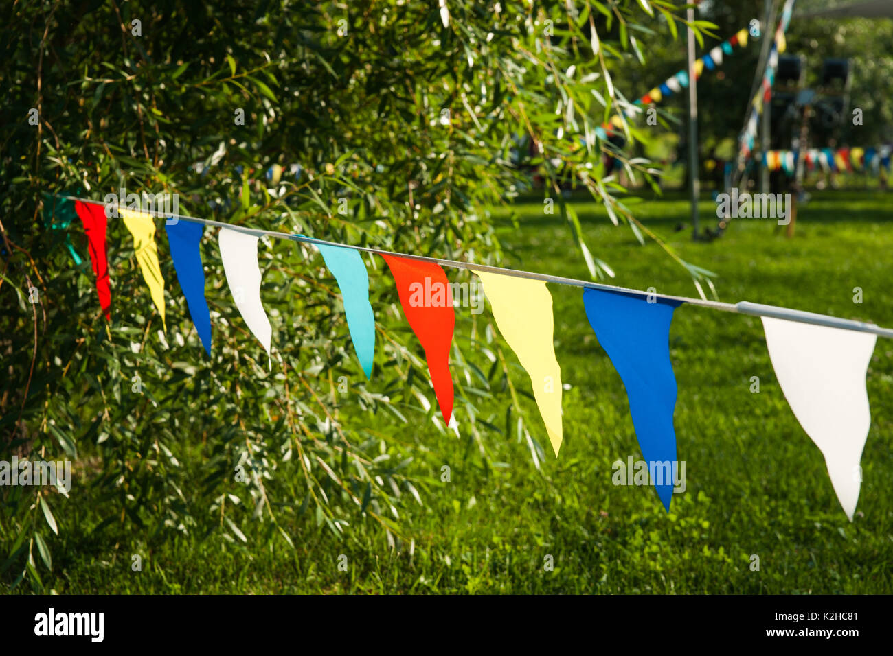 Rot, Weiß, Blau, Gelb, Grün Dreieck Wimpelketten hängend an einem Seil in den Park gegen das grüne Gras, baum laub. Stockfoto