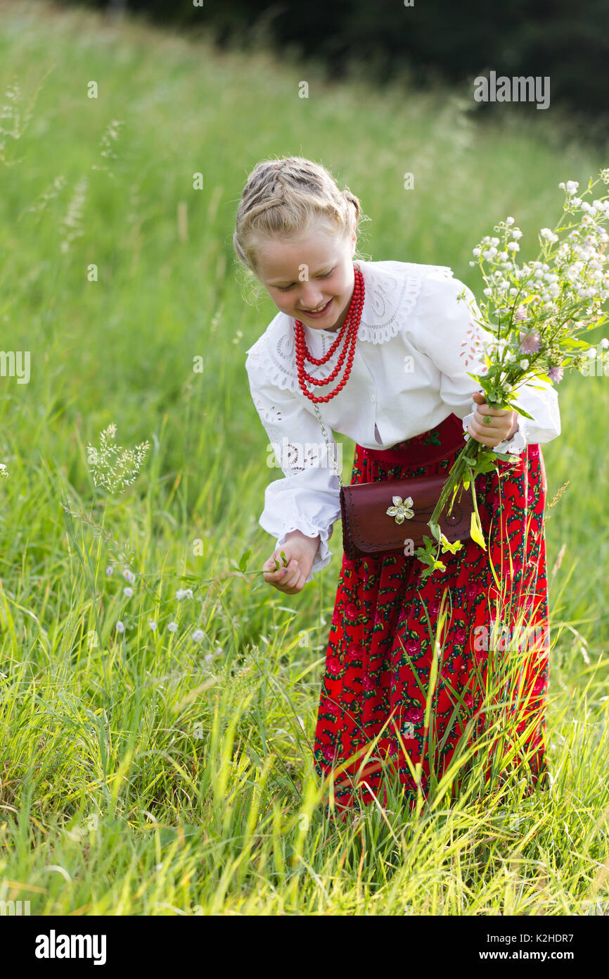 Junge lächelnde Mädchen in traditionellen polnischen Berg Leute kleiden Kommissionierung Blume in den Bergen Wiese. Vertikale ehrliches Porträt im Morgenlicht Stockfoto