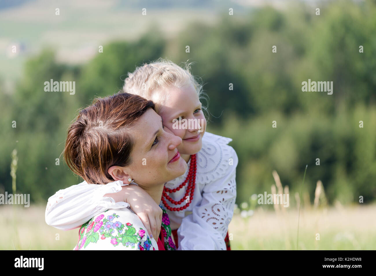 Tochter dressing traditioneller Folk dress umarmen Mama auf Wiese in polnischen Bergen. In der Nähe der horizontalen Porträt im sonnigen Morgen Stockfoto