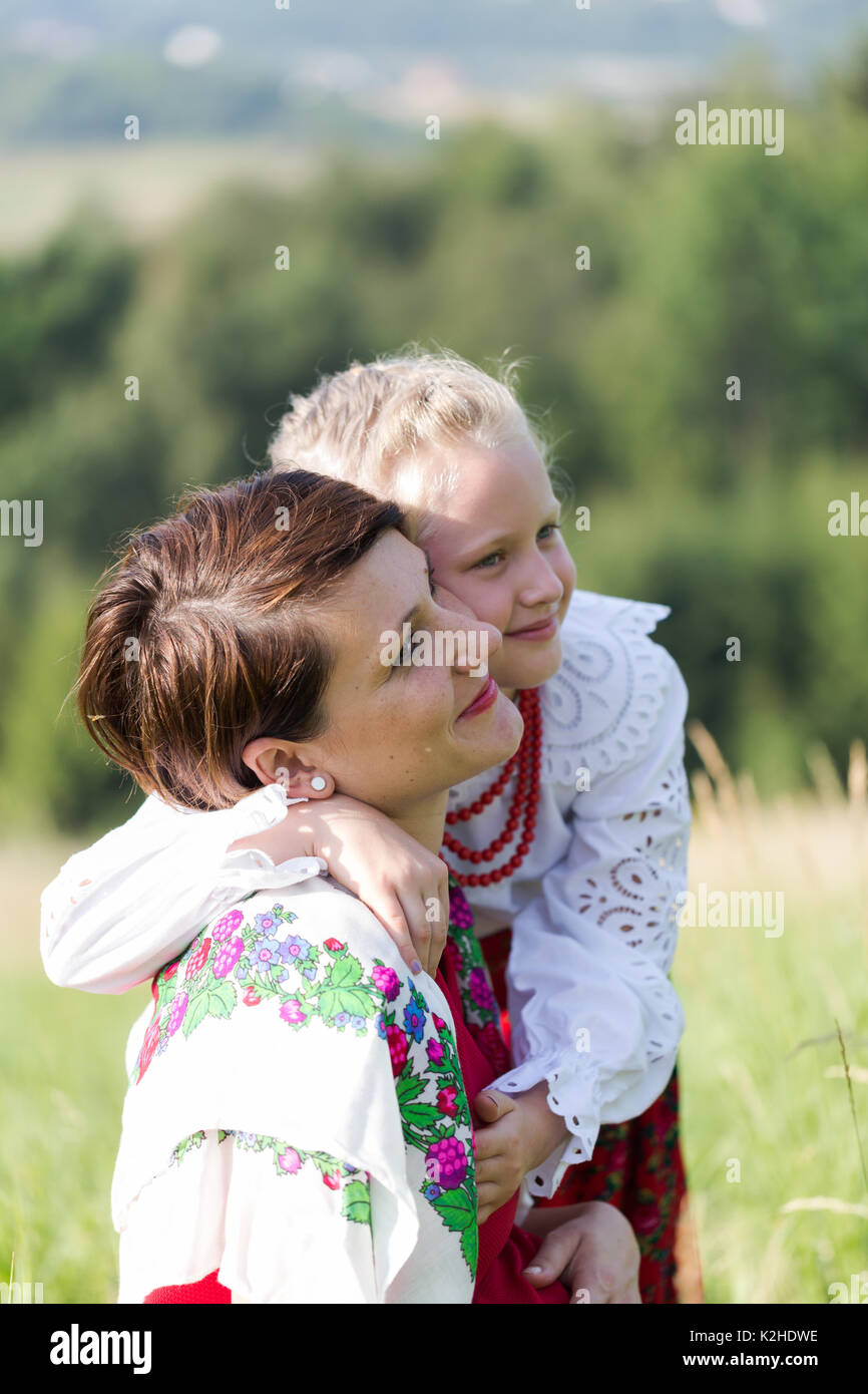 Tochter dressing traditioneller Folk dress umarmen Mama auf Wiese in polnischen Bergen. Close up vertikale Porträt im sonnigen Morgen Stockfoto