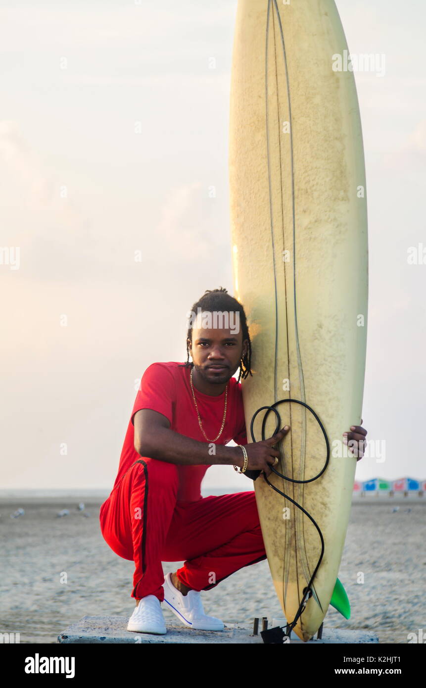 Afrikanische amerikanische Mann mit Surfbrett am Strand Stockfoto