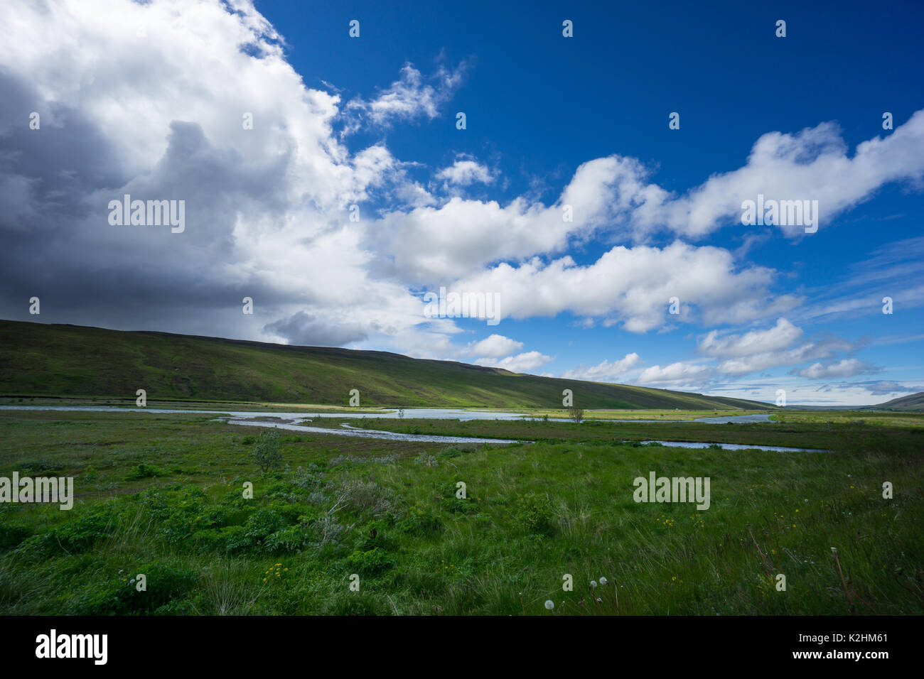 Island - Natürliche Flusslauf durch unberührte weite grüne Landschaft mit ankommenden Gewitter Stockfoto