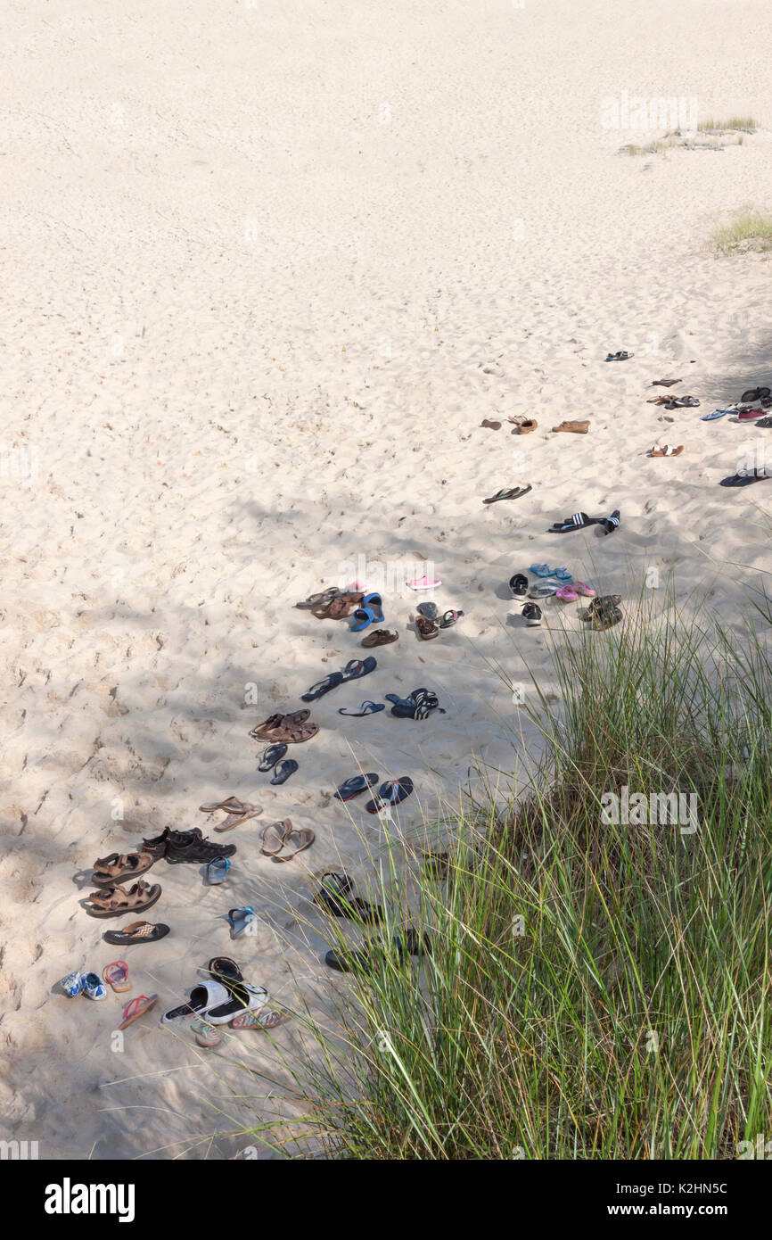 Sandalen, Flip Flops und Schuhe in den Sand links von barfuß Beachgoers. Stockfoto