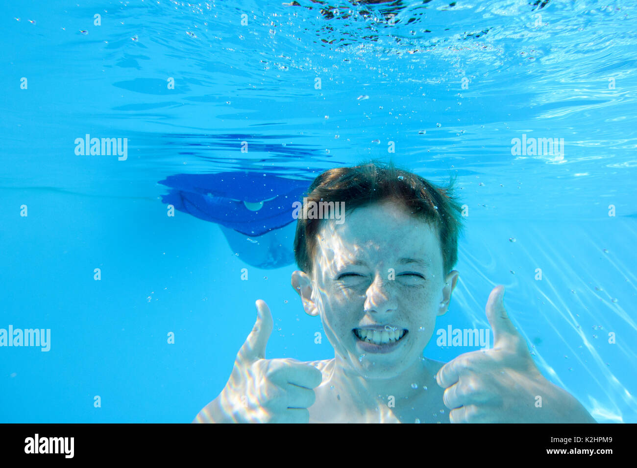 Auburn behaartes Jugendjungen, Daumen hoch, während unter Wasser im Schwimmbad, Blick in die Kamera Stockfoto
