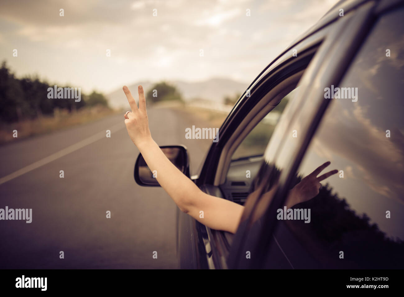 Junge glücklich Frau fährt ein Auto und macht OK Zeichen mit der Hand aus dem Auto. Freiheit, Reisen und Exploration Konzept. Stockfoto