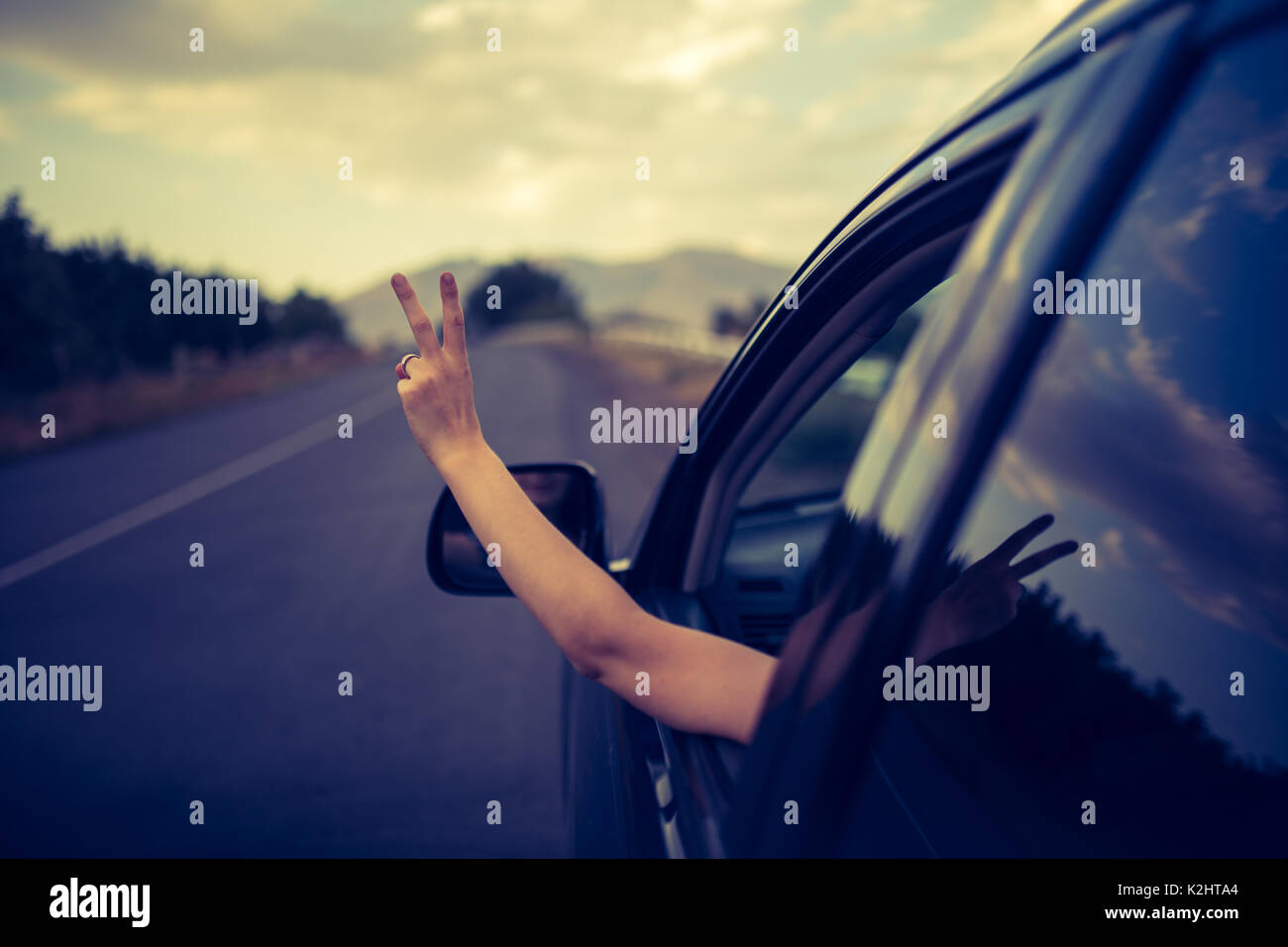 Junge glückliche junge Mädchen fährt ein Auto eine Hand aus dem Fenster heraus hält. Lady Fahrer fahren und zeigt OK Zeichen mit der Hand aus dem Fenster. Stockfoto