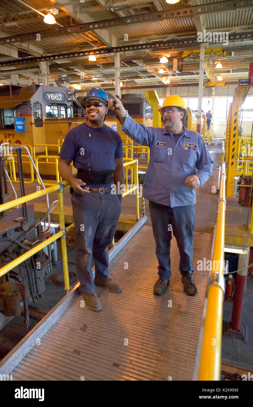 Eine afrikanische amerikanische Eisenbahn Wartung Arbeiter erhält Arbeitsanweisungen von seiner kaukasischen Chef an einem Eisenbahn Güterbahnhof Reparatur Schuppen in Roseville, CA. Hinweis Lok im Hintergrund. MODEL RELEASE Stockfoto