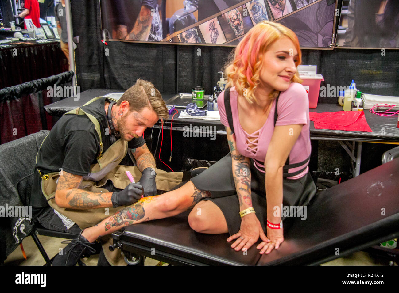 Eine glückliche junge Frau hat ein Tattoo am Bein gezeichnet von einem tätowierer auf einem Kongress in Costa Mesa, CA. Beachten Sie Gummihandschuhe. Stockfoto