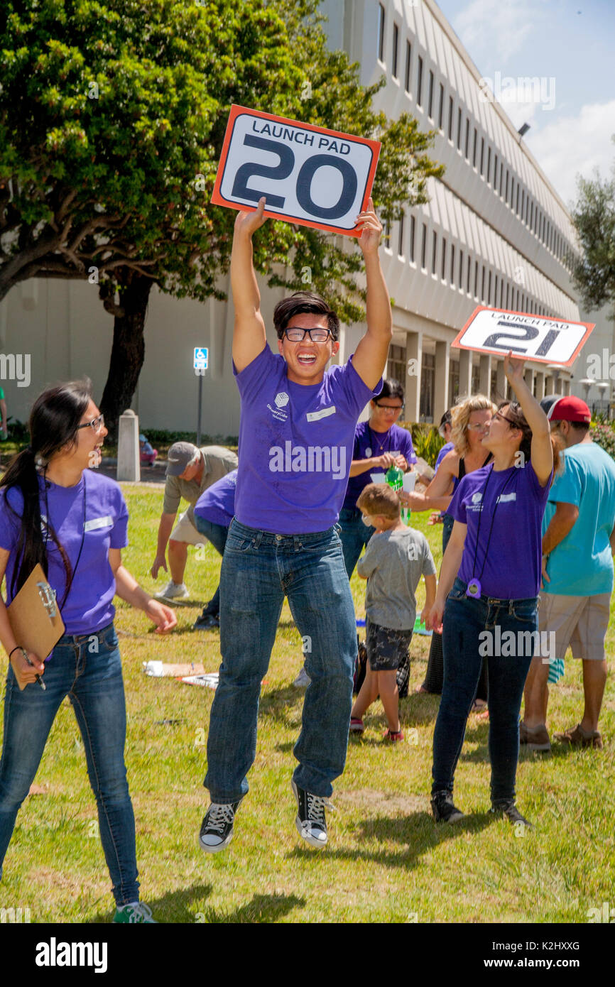 Eine asiatische amerikanische junge erwachsene Ausbilder an einer Wasserrakete Festival in Huntington Beach, CA, hält eine Anzahl Zeichen, da springt er Teilnehmer zu informieren, das er bereit ist eine weitere Rakete zu starten. Hinweis Schutzbrille und einheitliche T-Shirts. Stockfoto