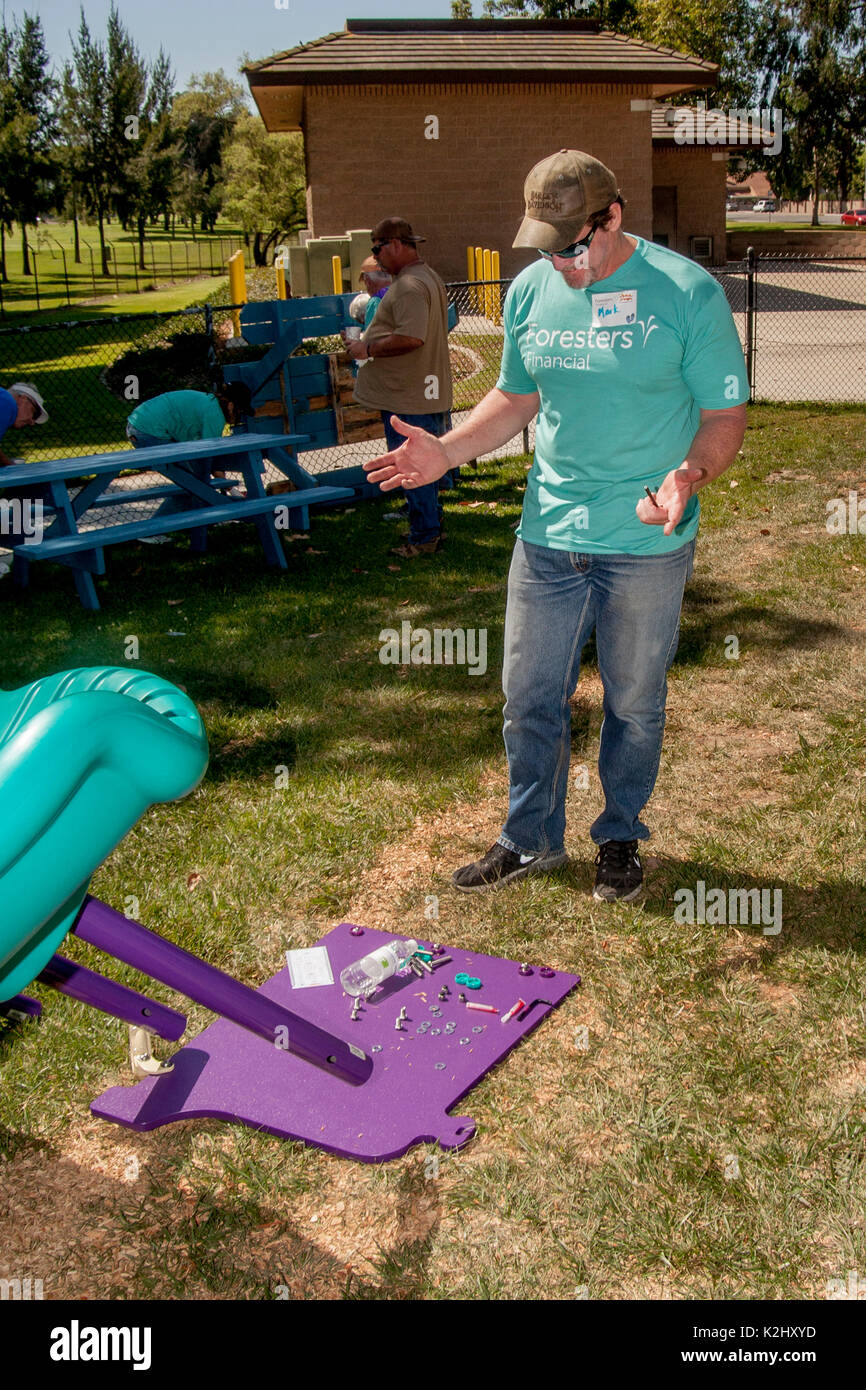 Ein freiwilliger Arbeiter scheint von der Gruppe der Teile, die notwendig sind, um eine Rutschbahn in einem Park in Fountain Valley, CA zu montieren frustriert. Hinweis: T-Shirt mit Logo. Stockfoto