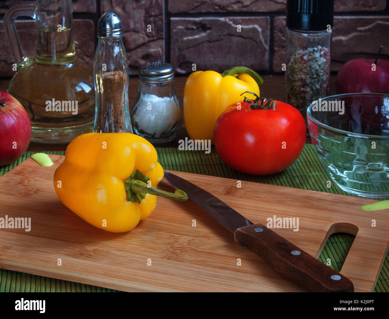 Große saftige gelbe Paprika auf einem hölzernen Schneidebrett auf einem Tisch mit roten Tomaten, Äpfel, Pflanzenöl, Salz, Gewürze Stockfoto