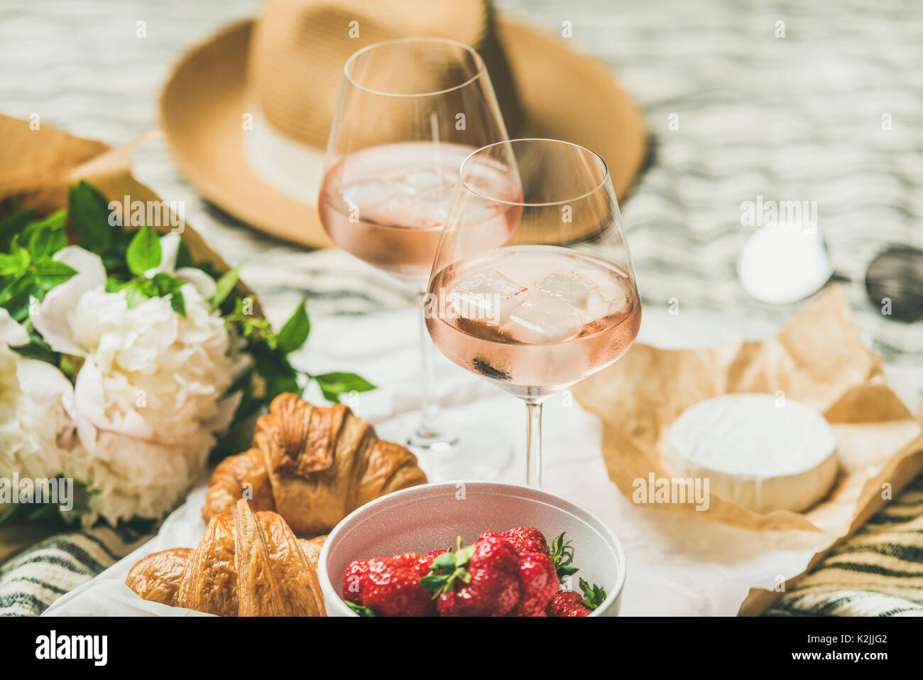 Im französischen Stil romantisch Sommer Picknick Einstellung. Flachbild-lay Gläser rose Wein mit Eis, frischen Erdbeeren, Croissants, Brie Käse, Strohhut, sungla Stockfoto