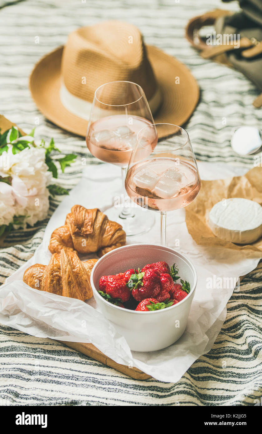 Im französischen Stil romantisch Sommer Picknick Einstellung. Flachbild-lay Gläser rose Wein mit Eis und Erdbeeren, die in der Schüssel, Croissants, Brie Käse, Strohhut, peon Stockfoto