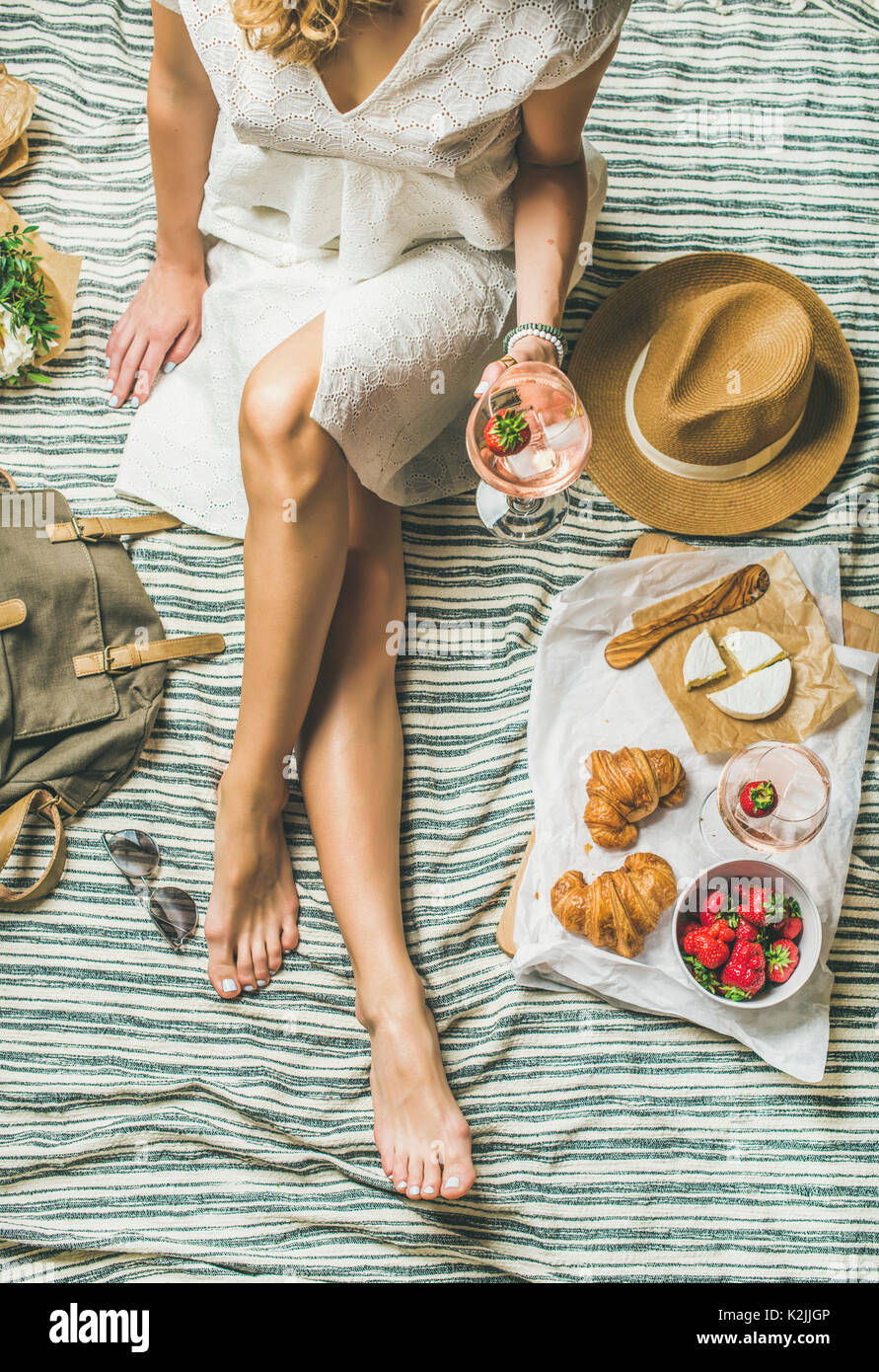 Im französischen Stil romantisches Picknick. Frau im Kleid mit Glas Wein, Erdbeeren, Croissants, Brie Käse, Sonnenbrille, Stroh, Hut, Pfingstrose Blumen o Stockfoto