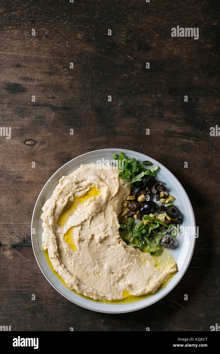 Hausgemachte, traditionelle Verbreitung Hummus mit Hacken, Oliven und Kräutern auf blauen Platte, diente über alte Holz- Hintergrund. Mediterrane Snacks. Flach, cop Stockfoto