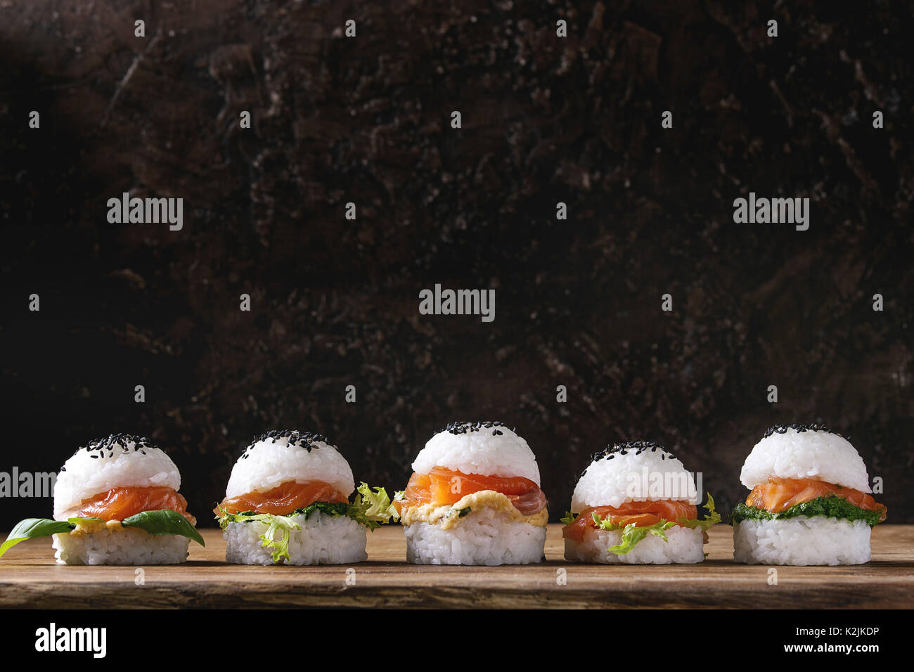 Mini Reis sushi Burger mit geräuchertem Lachs, grüner Salat und Saucen, schwarzer Sesam mit Stäbchen aus Holz Über Holz Hintergrund serviert. Moderne gesunde fo Stockfoto