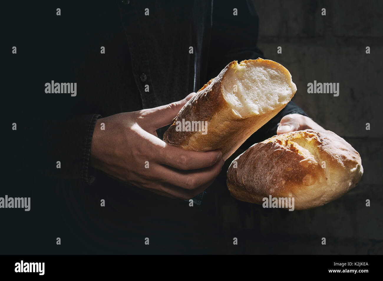 Laib von frisch gebackenem Brot aus Weizen in den Händen des Menschen in der Sonne. Rustikale Tag Licht in dunklen Zimmer. Getonten Bild Stockfoto