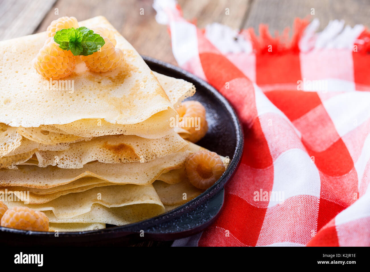 Hausgemachte crepes serviert mit frischem Gelb Himbeeren in Gusseisen Skillet für romantische Brunch am rustikalen Tisch witn rot-karierten Tischtuch Stockfoto