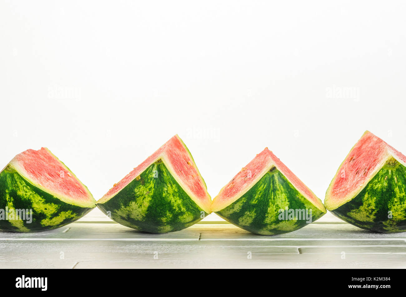 Vier Scheiben eine Wassermelone liegen in einer Reihe auf weiße Holztisch auf weißem Hintergrund. Minimalistische leere Hintergrund Stockfoto